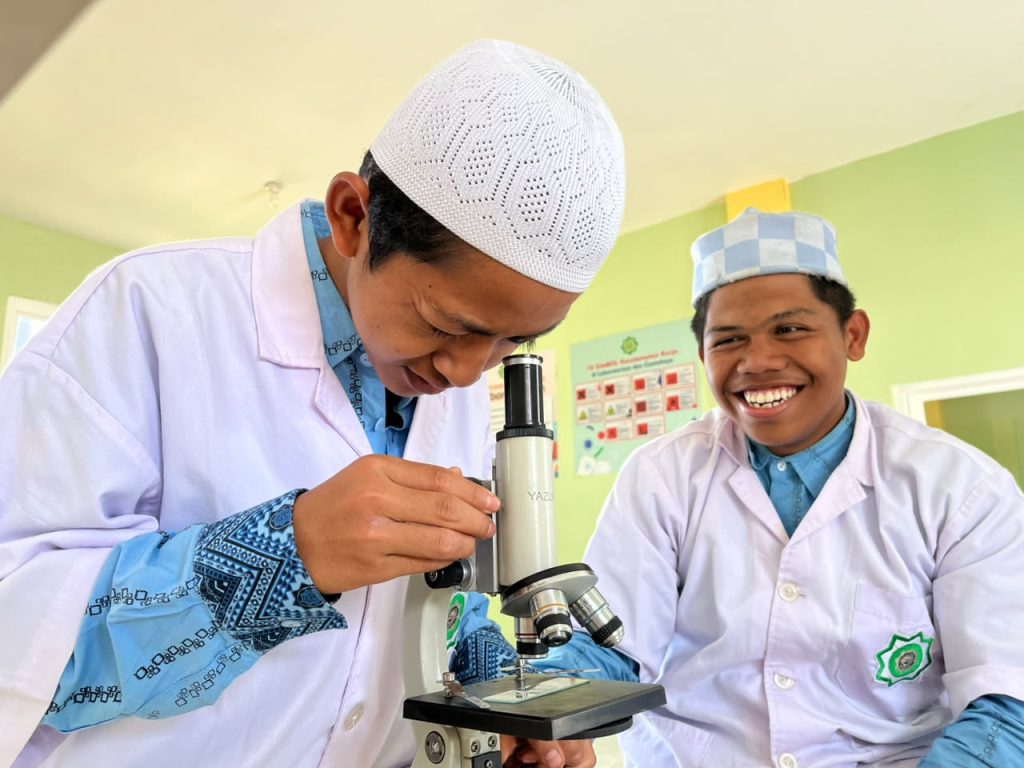 Santri putra Kelas 10 Sains eLKISI mengamati jamur pada tempe busuk menggunakan mikroskop dalam praktikum Biologi.